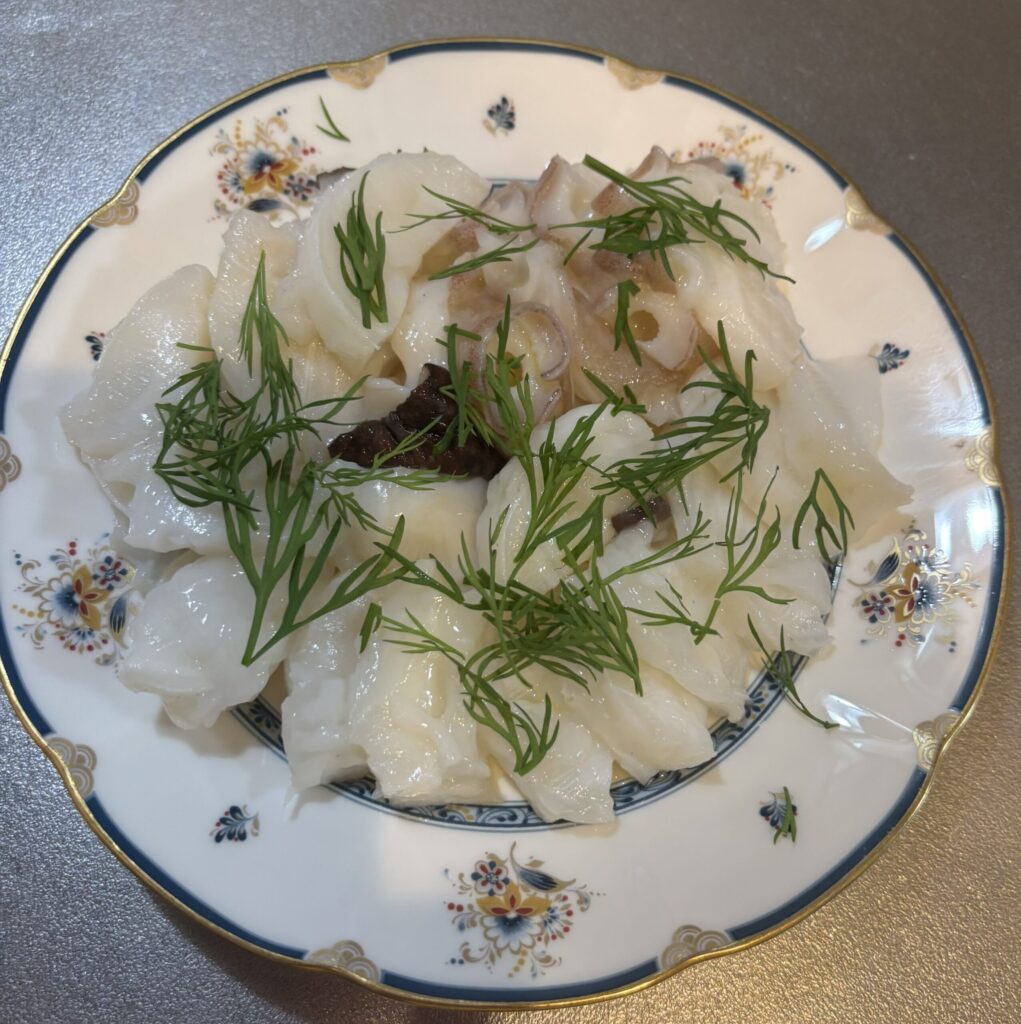 完成したタコのマリネを切って盛り付けた様子。上にディルの葉が散りばめられている。